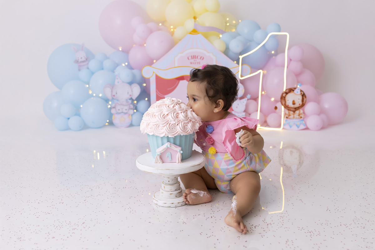 Bebê em ensaio Smash the Cake tema circo em estúdio fotográfico em Caraguatatuba, cenário colorido personalizado, bolo decorado, criança sorrindo e se divertindo durante sessão infantil