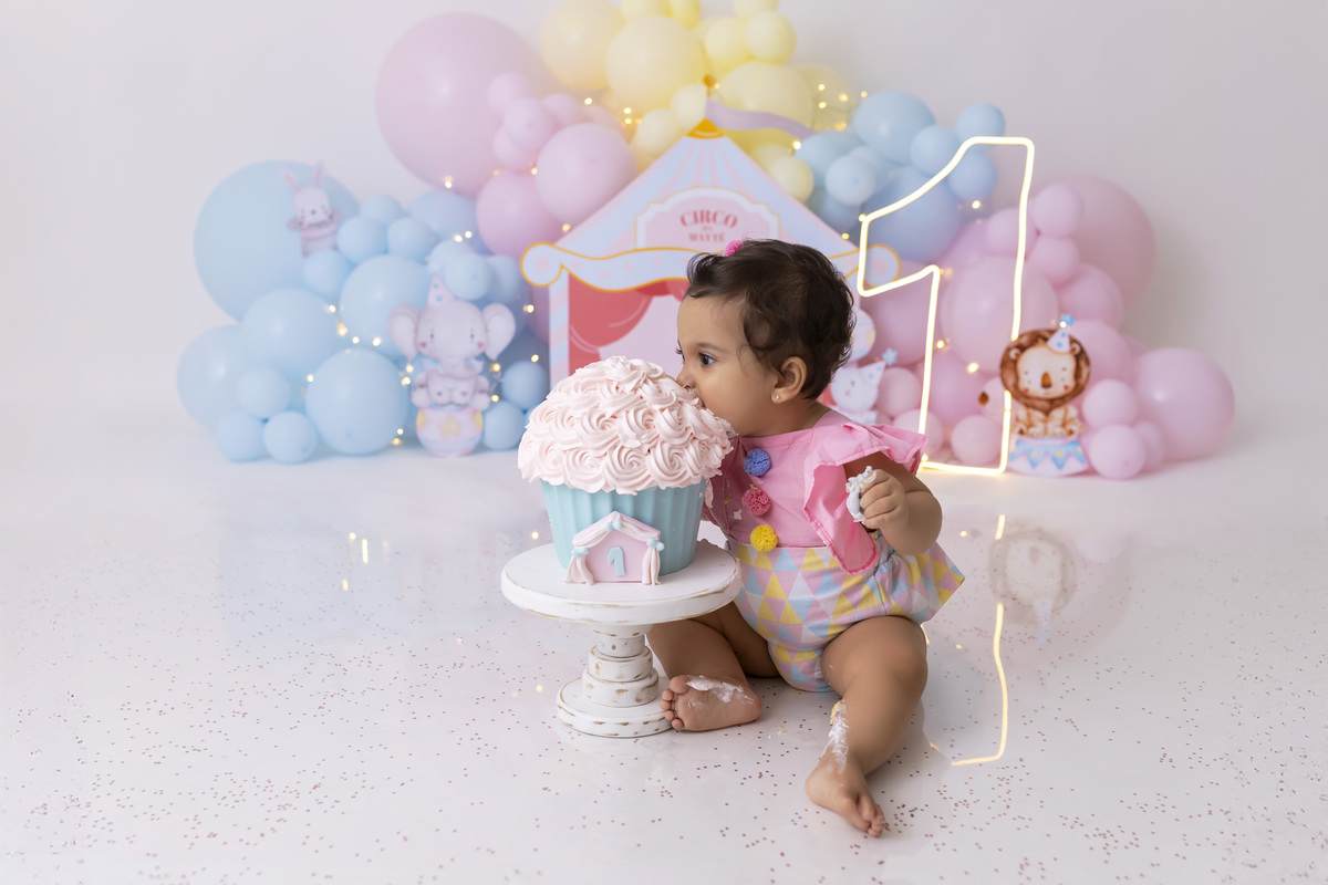 Bebê em ensaio Smash the Cake tema circo em estúdio fotográfico em Caraguatatuba, cenário colorido personalizado, bolo decorado, criança sorrindo e se divertindo durante sessão infantil