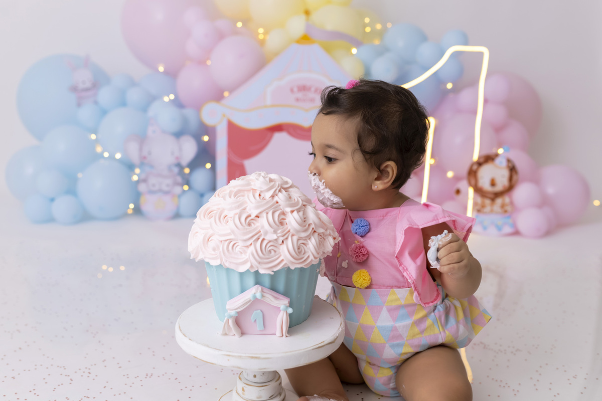 Bebê em ensaio Smash the Cake tema circo em estúdio fotográfico em Caraguatatuba, cenário colorido personalizado, bolo decorado, criança sorrindo e se divertindo durante sessão infantil