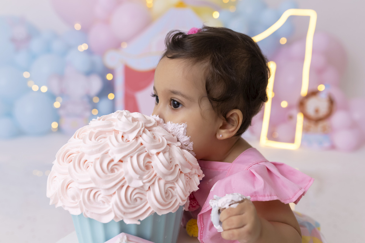 Bebê em ensaio Smash the Cake tema circo em estúdio fotográfico em Caraguatatuba, cenário colorido personalizado, bolo decorado, criança sorrindo e se divertindo durante sessão infantil