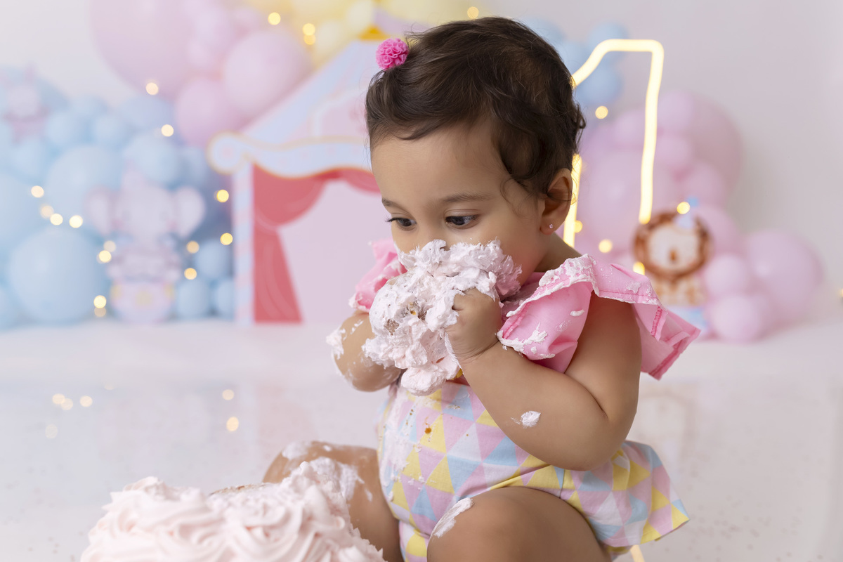 Bebê em ensaio Smash the Cake tema circo em estúdio fotográfico em Caraguatatuba, cenário colorido personalizado, bolo decorado, criança sorrindo e se divertindo durante sessão infantil