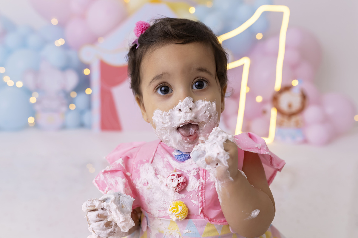 Bebê em ensaio Smash the Cake tema circo em estúdio fotográfico em Caraguatatuba, cenário colorido personalizado, bolo decorado, criança sorrindo e se divertindo durante sessão infantil