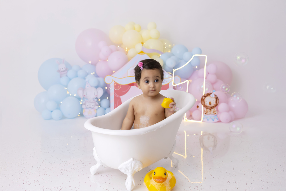 Bebê em ensaio Smash the Cake tema circo em estúdio fotográfico em Caraguatatuba, cenário colorido personalizado, bolo decorado, criança sorrindo e se divertindo durante sessão infantil