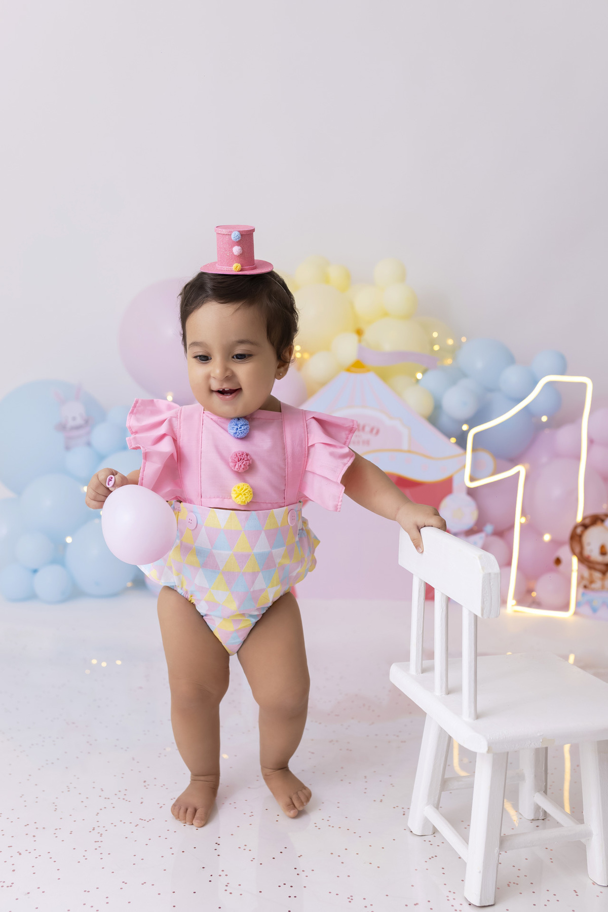 Bebê em ensaio Smash the Cake tema circo em estúdio fotográfico em Caraguatatuba, cenário colorido personalizado, bolo decorado, criança sorrindo e se divertindo durante sessão infantil