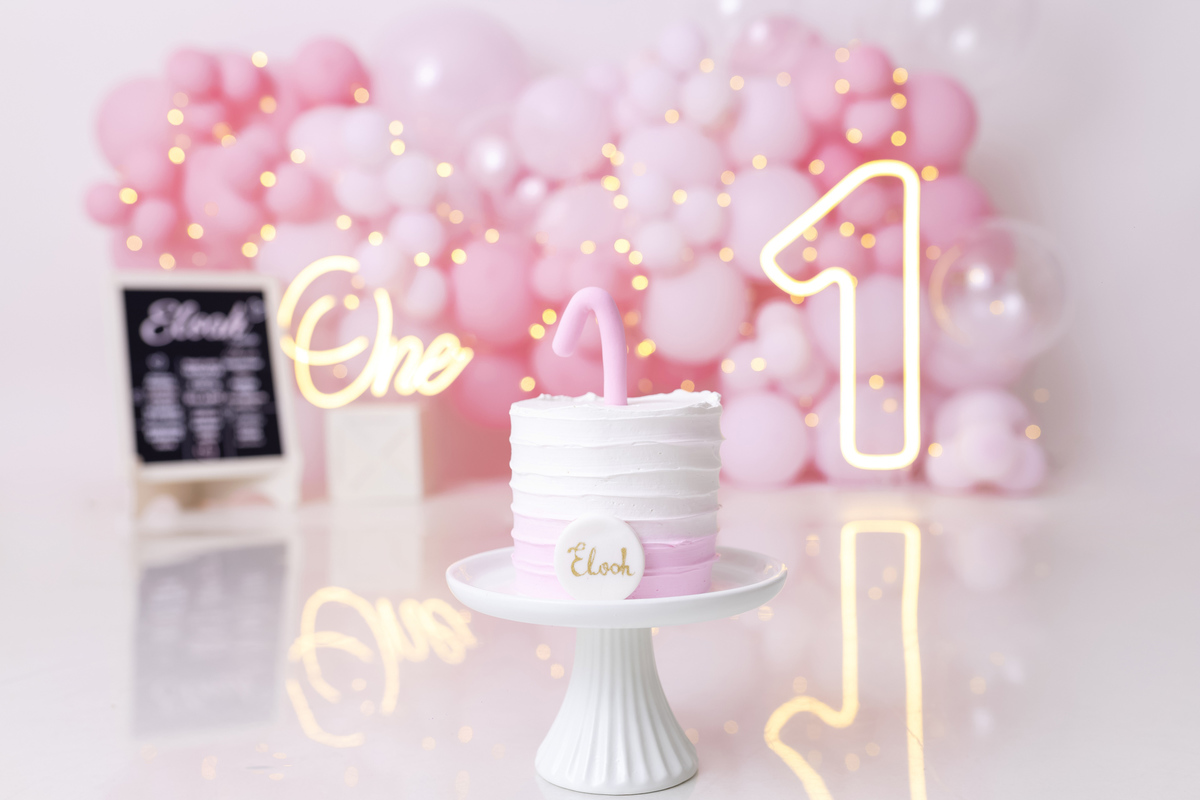 Bebê em ensaio Smash the Cake tema princesa rosa em estúdio fotográfico em Caraguatatuba, cenário delicado, vestido rosa, bolo personalizado e criança sorrindo enquanto brinca com o bolo