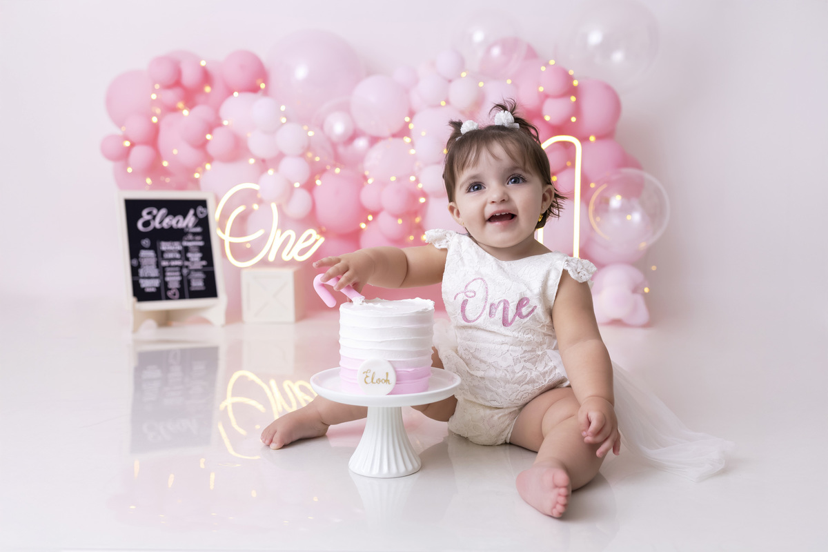 Bebê em ensaio Smash the Cake tema princesa rosa em estúdio fotográfico em Caraguatatuba, cenário delicado, vestido rosa, bolo personalizado e criança sorrindo enquanto brinca com o bolo