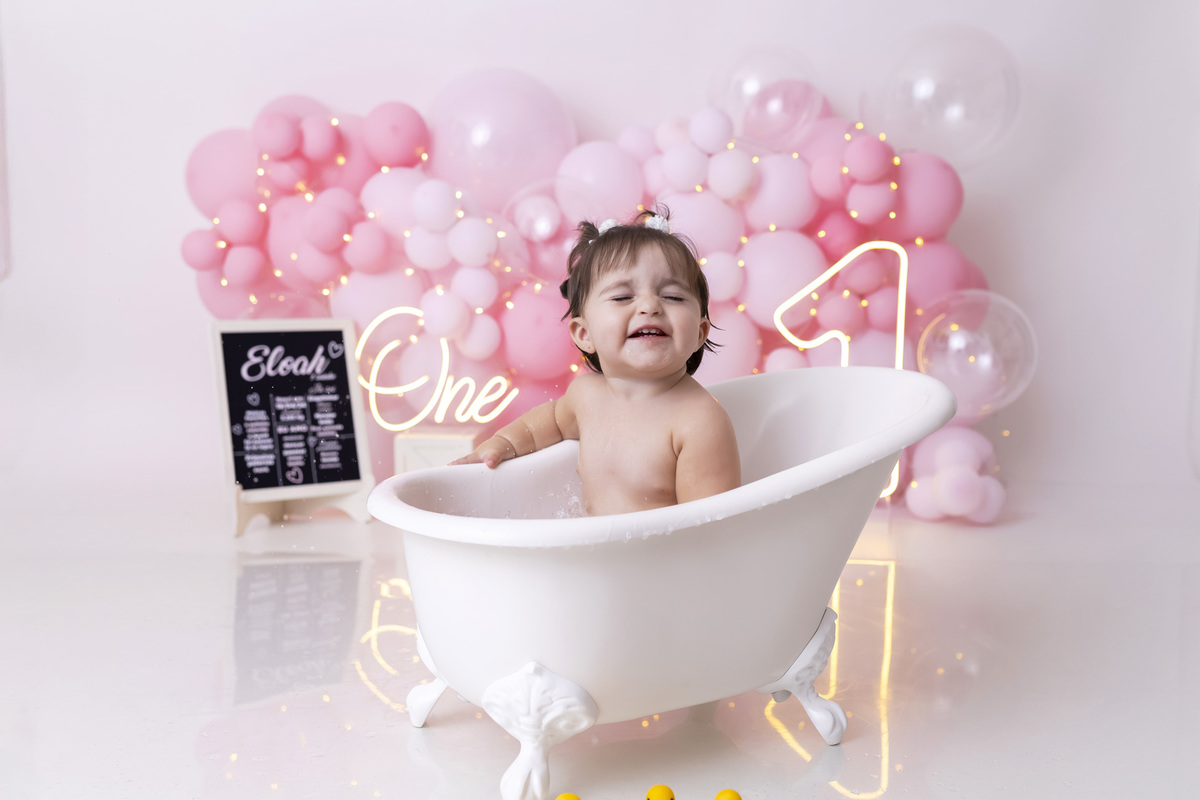 Bebê em ensaio Smash the Cake tema princesa rosa em estúdio fotográfico em Caraguatatuba, cenário delicado, vestido rosa, bolo personalizado e criança sorrindo enquanto brinca com o bolo