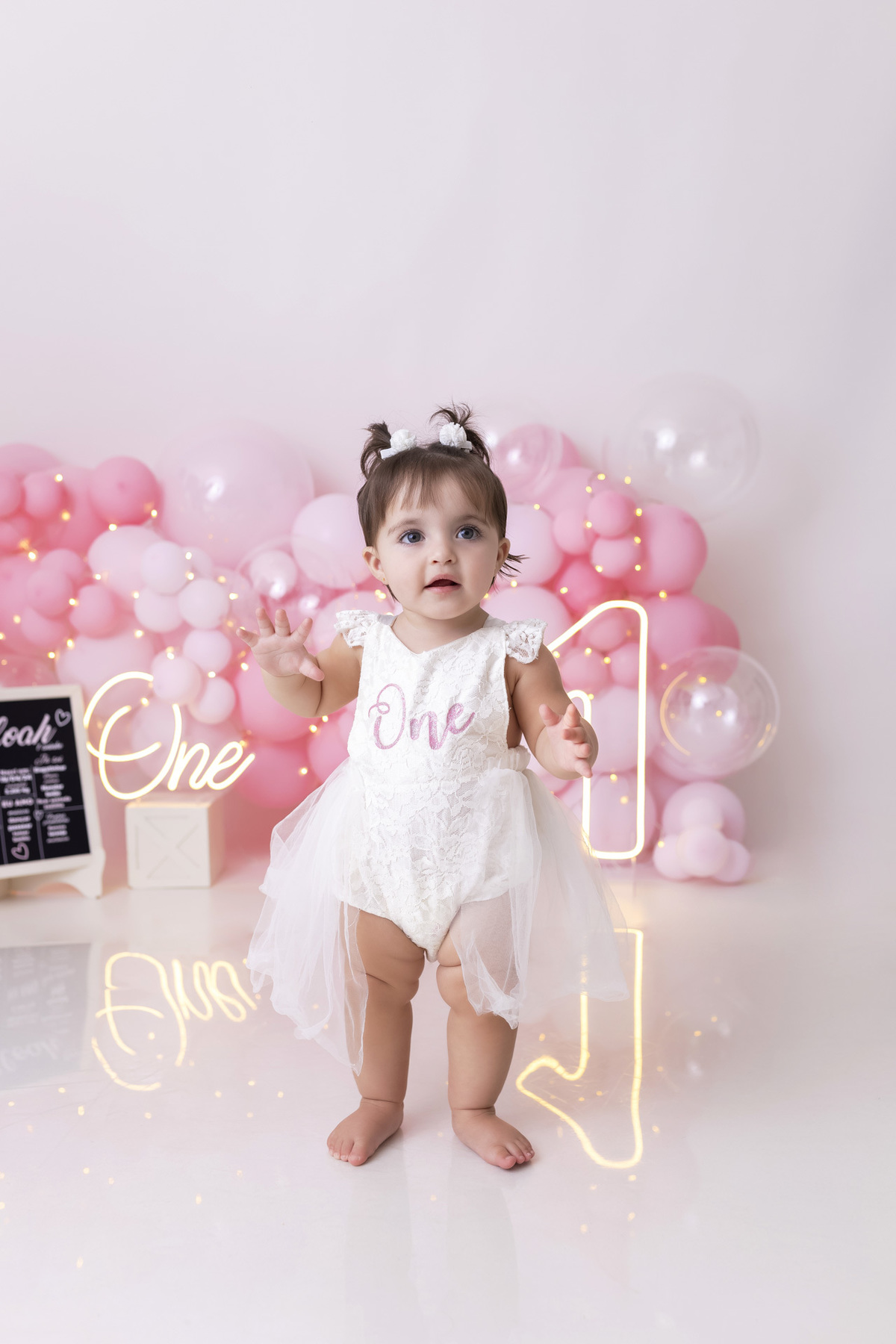 Bebê em ensaio Smash the Cake tema princesa rosa em estúdio fotográfico em Caraguatatuba, cenário delicado, vestido rosa, bolo personalizado e criança sorrindo enquanto brinca com o bolo