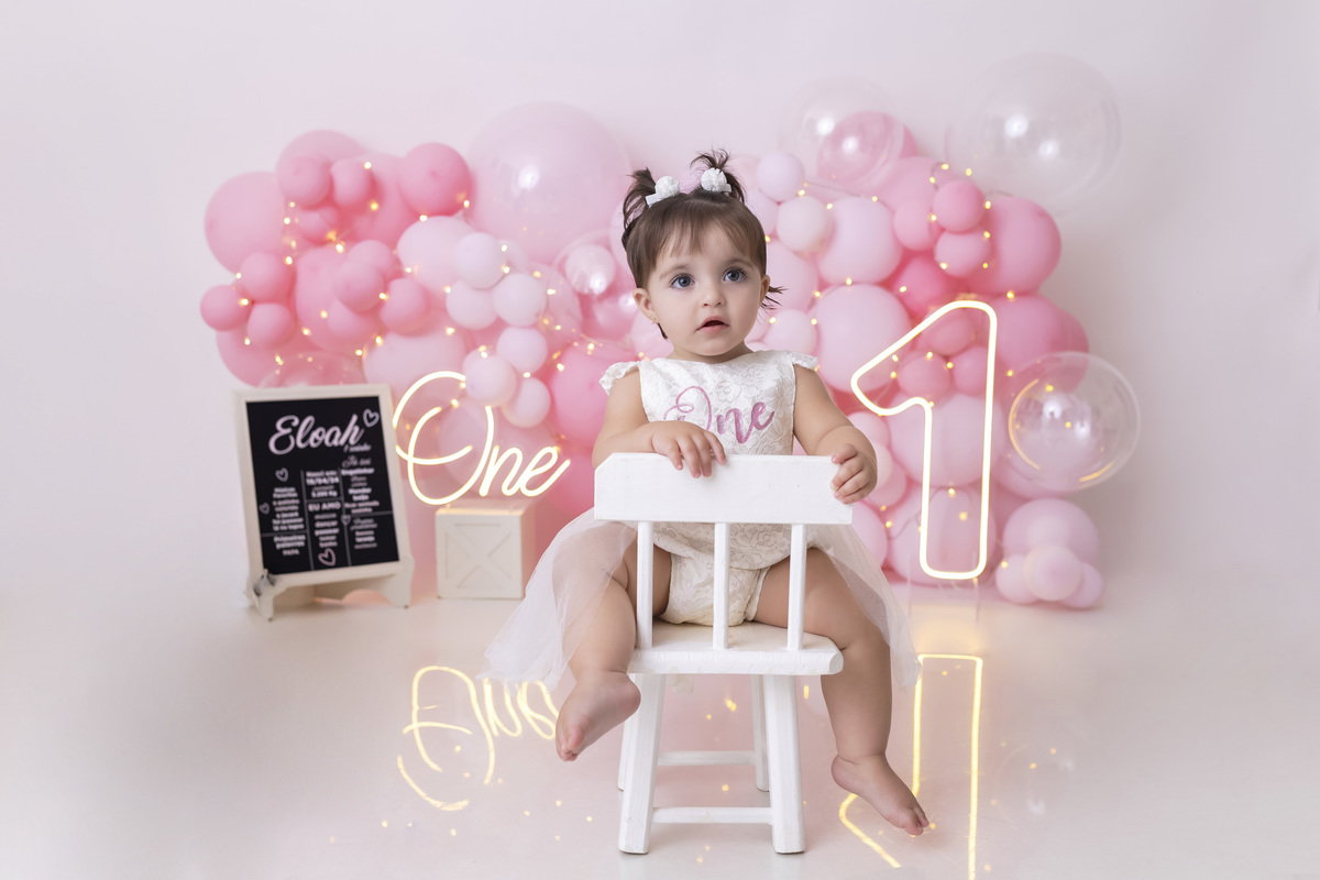 Bebê em ensaio Smash the Cake tema princesa rosa em estúdio fotográfico em Caraguatatuba, cenário delicado, vestido rosa, bolo personalizado e criança sorrindo enquanto brinca com o bolo