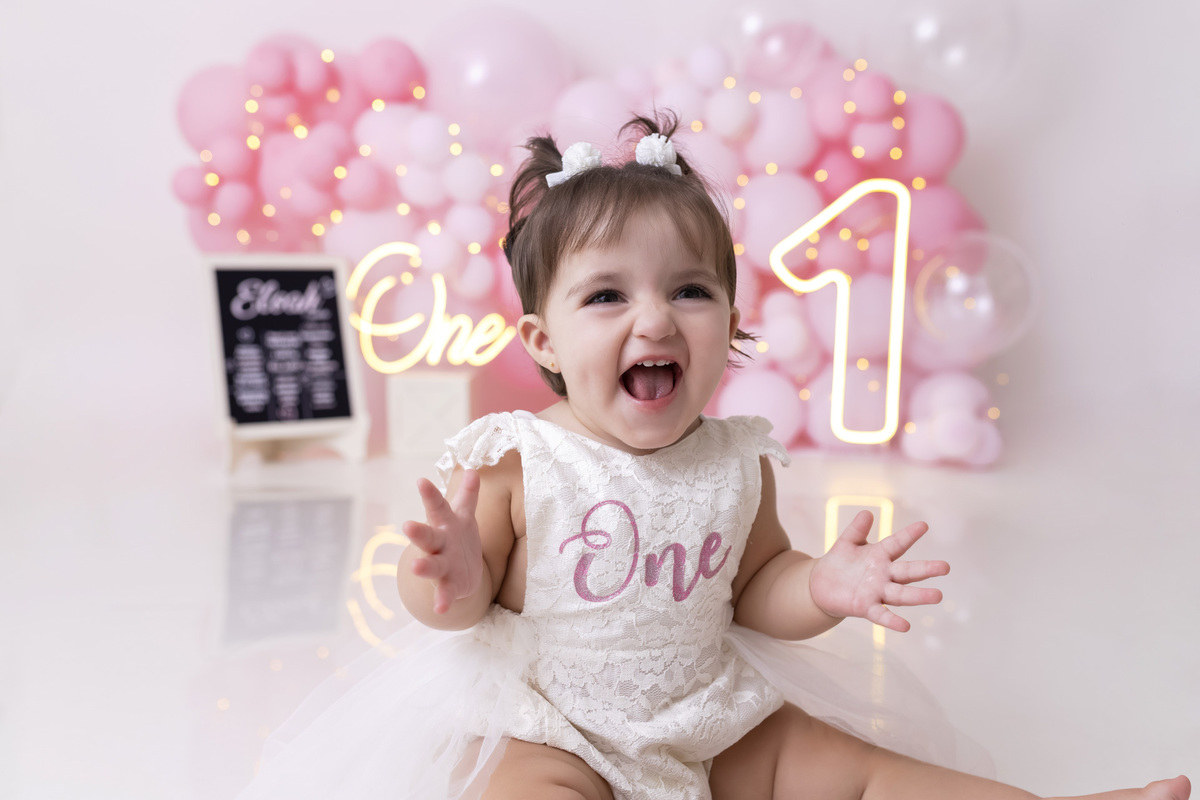 Bebê em ensaio Smash the Cake tema princesa rosa em estúdio fotográfico em Caraguatatuba, cenário delicado, vestido rosa, bolo personalizado e criança sorrindo enquanto brinca com o bolo