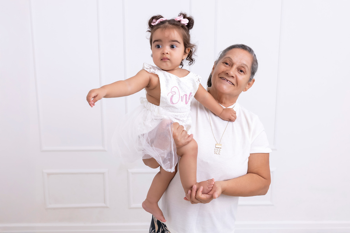 Bebê em ensaio Smash the Cake colorido com flores e raposinha em estúdio em Caraguatatuba, cenário personalizado em tons de rosa e laranja, criança sorrindo e brincando com o bolo de aniversário