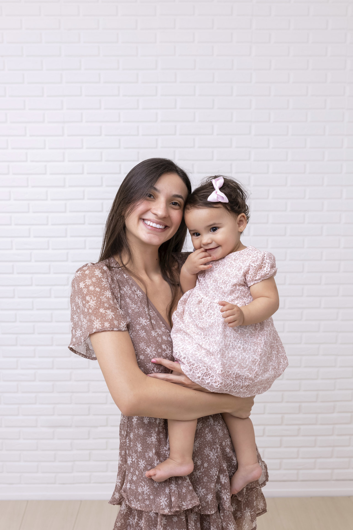 Bebê em ensaio Smash the Cake clean em estúdio branco com laços rosa, cenário minimalista e elegante, criança comendo e se lambuzando com bolo de aniversário em Caraguatatuba