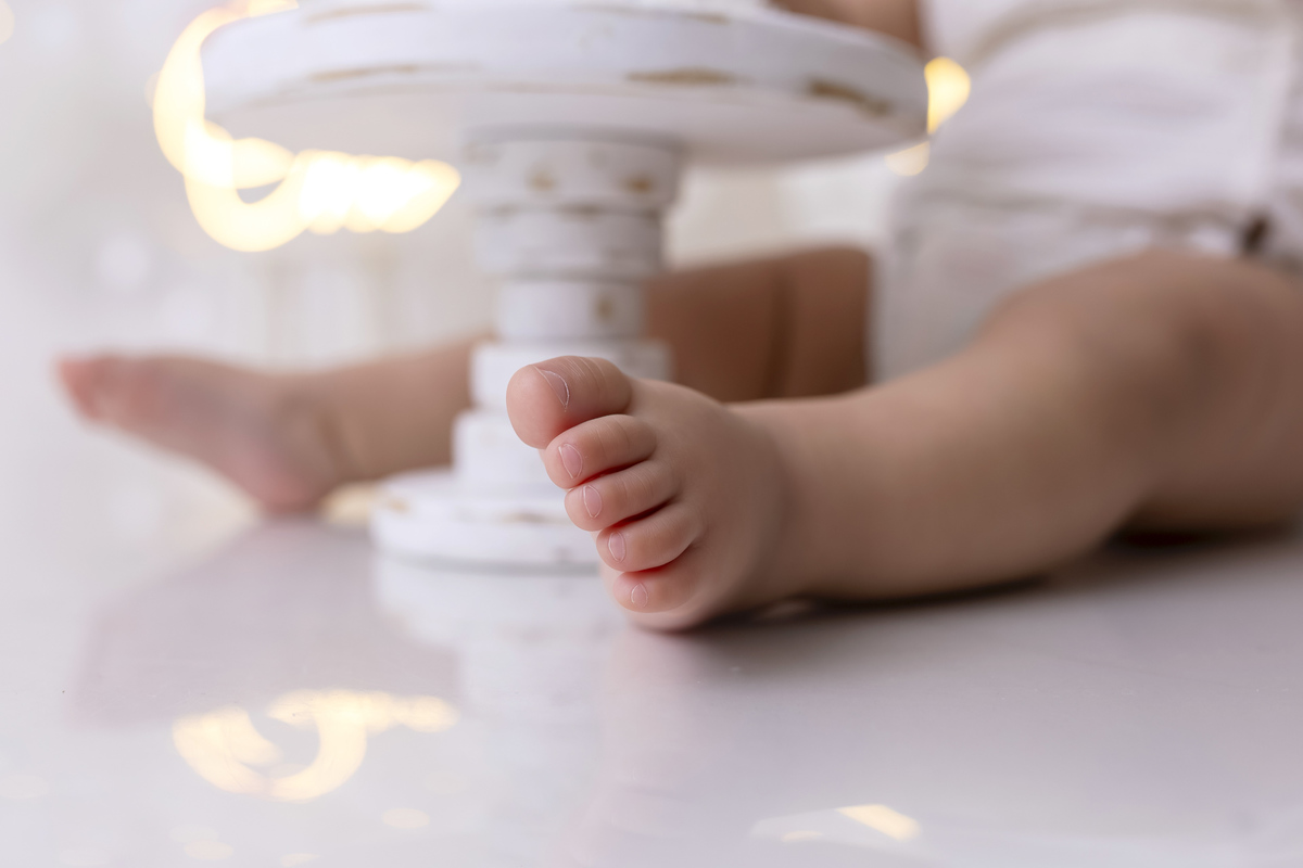 Bebê em ensaio Smash the Cake clean em estúdio branco com laços rosa, cenário minimalista e elegante, criança comendo e se lambuzando com bolo de aniversário em Caraguatatuba
