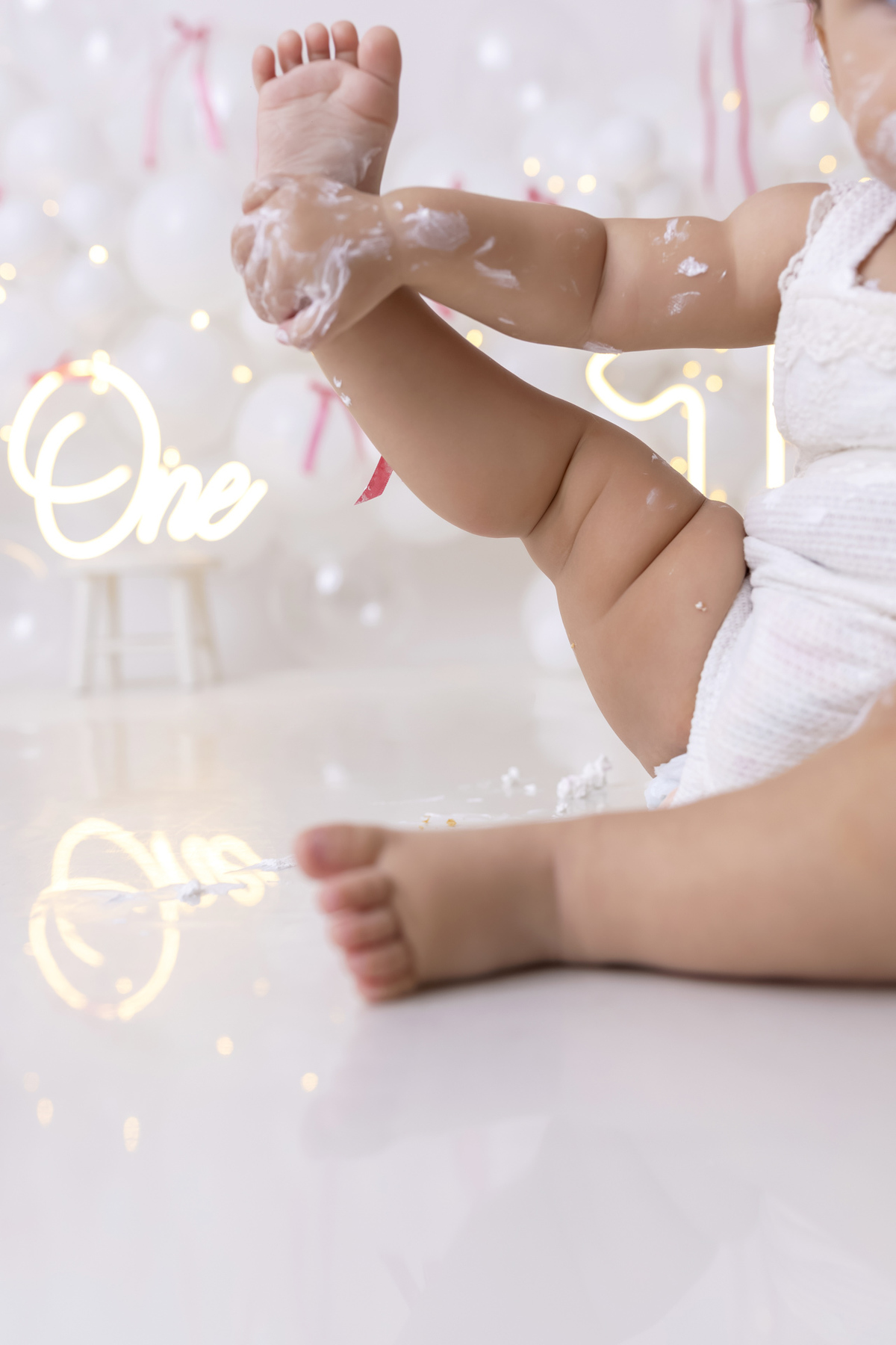 Bebê em ensaio Smash the Cake clean em estúdio branco com laços rosa, cenário minimalista e elegante, criança comendo e se lambuzando com bolo de aniversário em Caraguatatuba