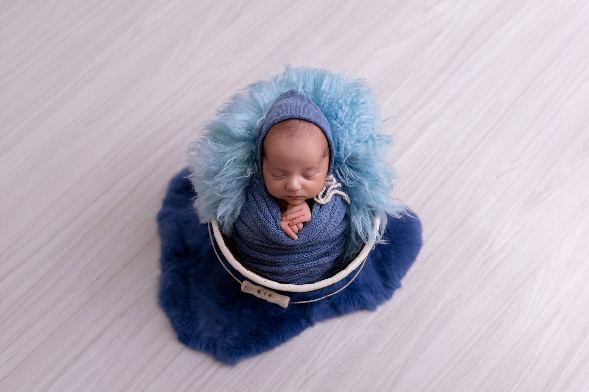 Bebê recém-nascido Levi enroladinho em tecido azul no baldinho durante ensaio newborn no estúdio On Click Fotografia em Caraguatatuba