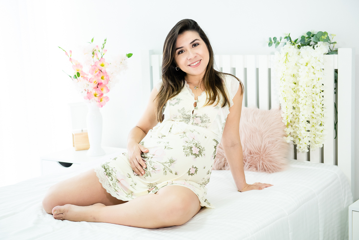 gestante fazendo pose com a mão na barriga sobre a cama branca em ensaio gestante gravida em