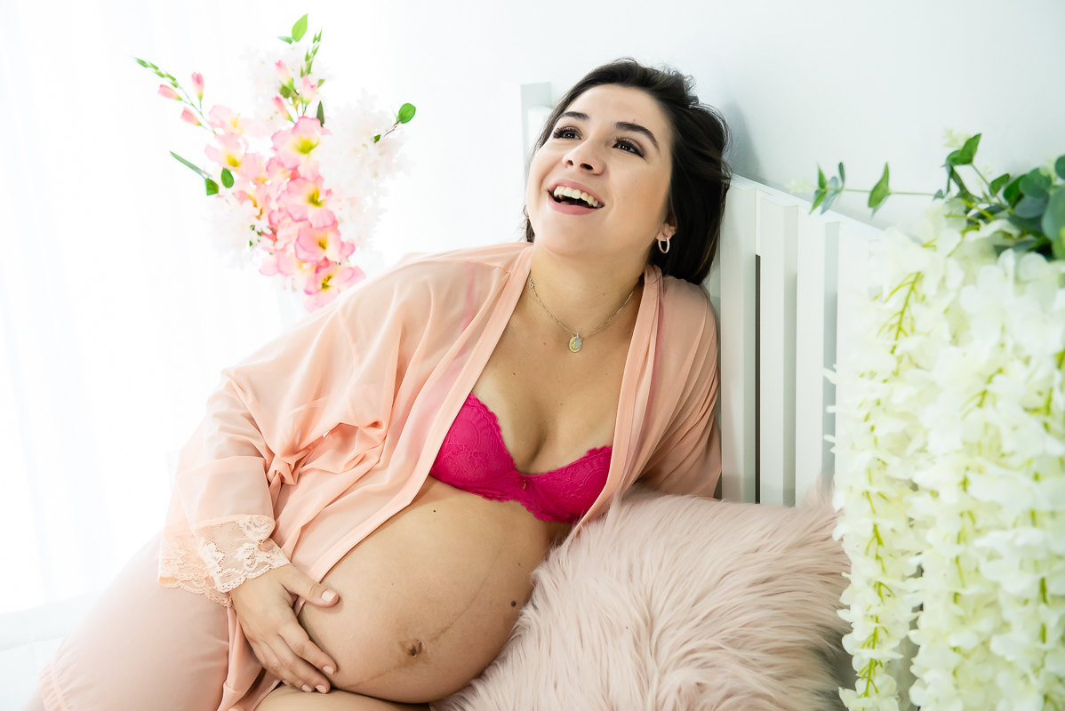gestante com a mão na barriga sentada na cama Ensaio gestante gravida em estúdio com luz natural