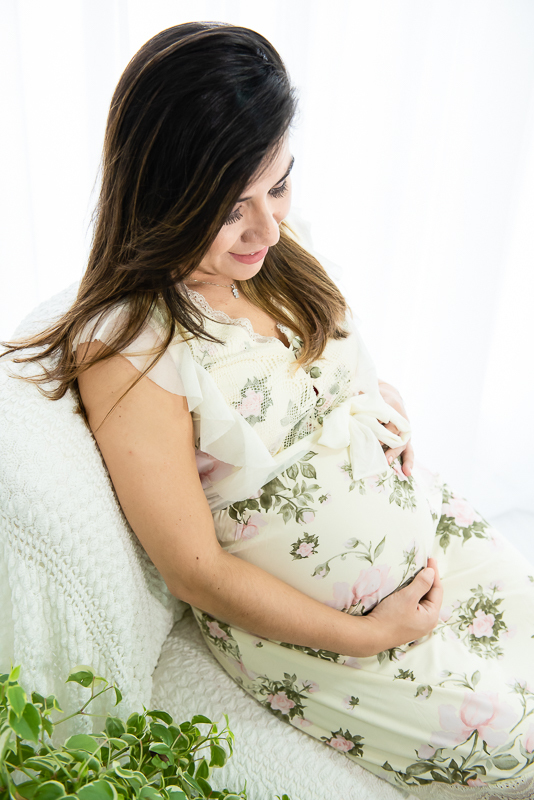 gestante sentada com vestido branco colocando a mão na barriga em ensaio gestante gravida em estúdio com luz natural