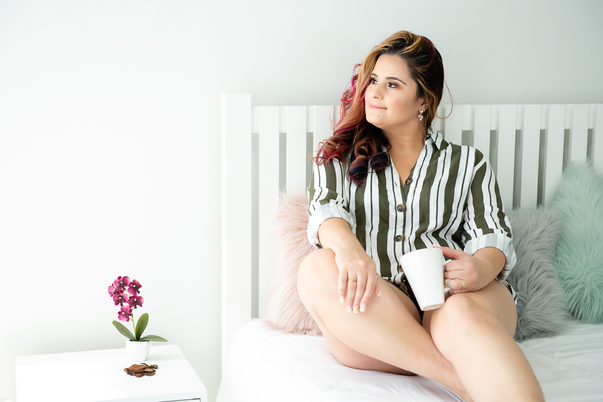 mulher madura sentada na cama segurando uma caneca posando para fotografia boudoir no rio de janeiro