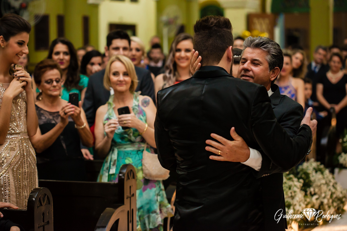 Pai da noiva emocionado abraça seu genro durante o casamento.