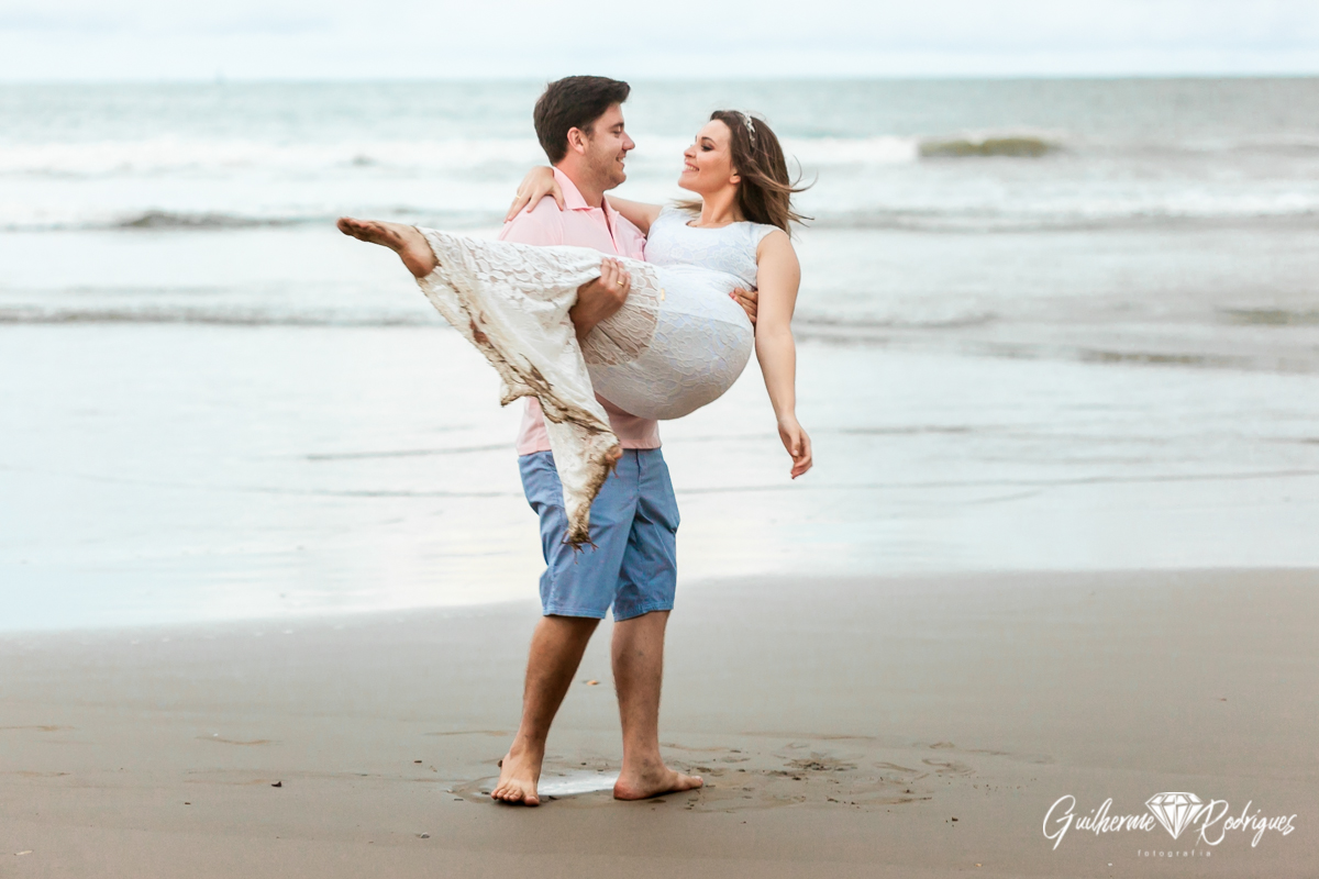 A noiva está no colo do seu noivo, noivos apaixonados na sessão de fotos do pré wedding na praia de Itajaí - SC. Fotógrafo de casamento de Itajaí Guilherme Rodrigues.