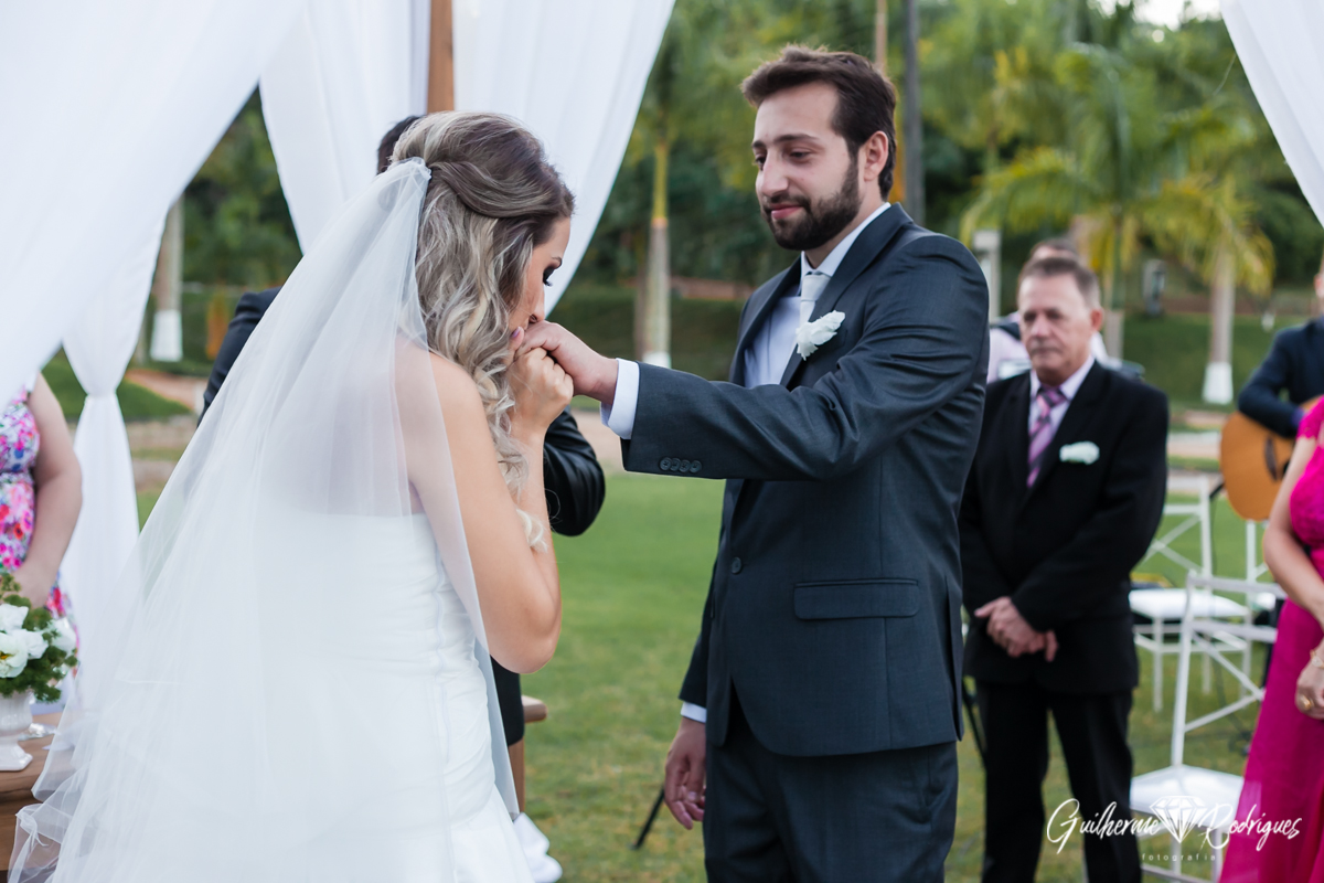 Troca das alianças. Noiva beija mão do noivo. Casamento de dia. Fotos Guilherme Rodrigues.