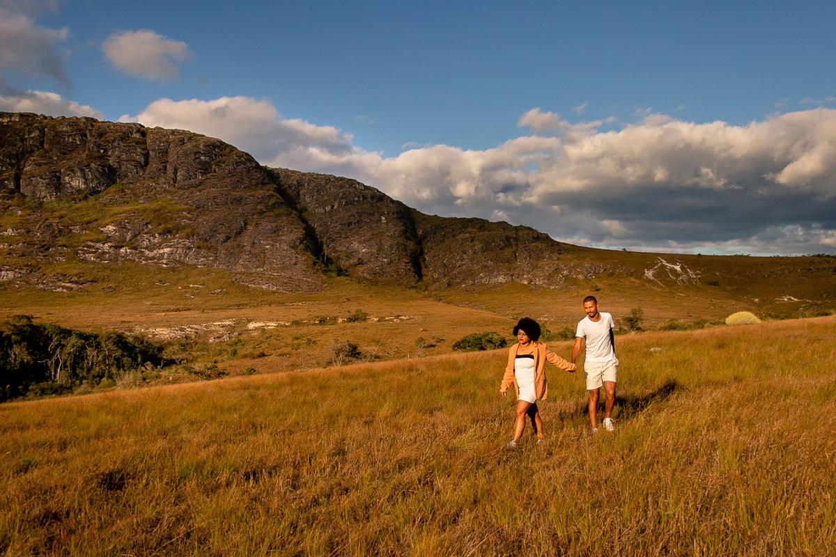 Casal andando na vegetação com uma montanha no fundo