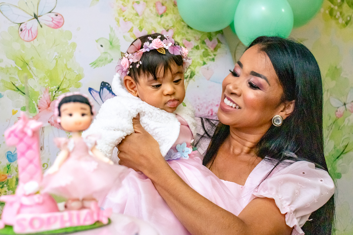 Mãe Sarah com sua filha Sophia nos braços atrás da velinha de aniversario de 1 ano