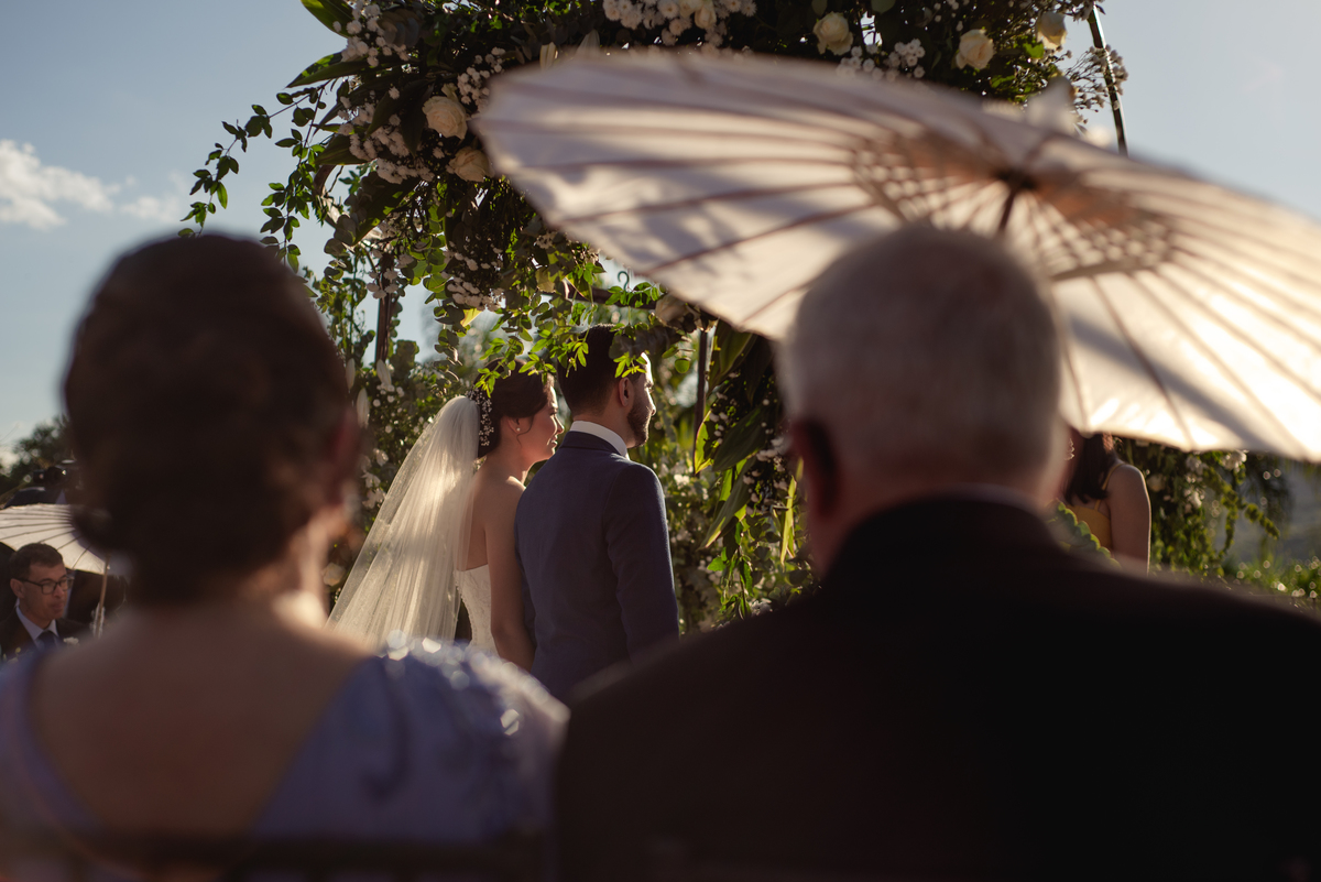 Casamento com muito sol e sombrinhas na cerimonia.