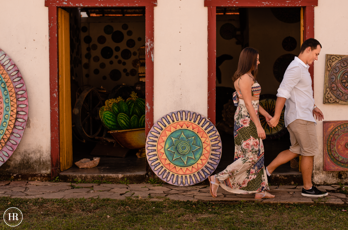 Casal caminhando em frente a loja de artesanato na cidade de Tiradentes no ensaio pre wedding.
