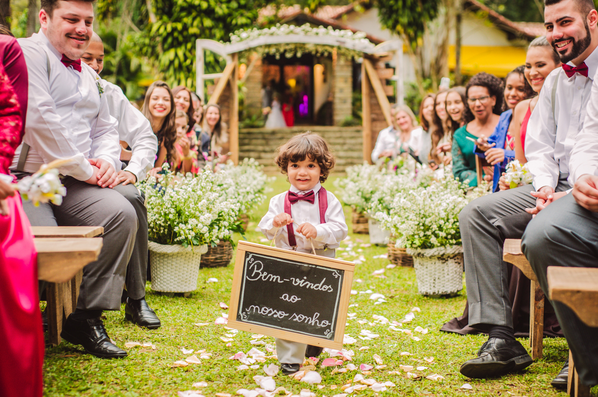 Foto de pajem com plaquinha no casamento realizado na Casa de Festas Riachos de Itaipava, em Petrópolis, RJ. Casamento diurno no campo.