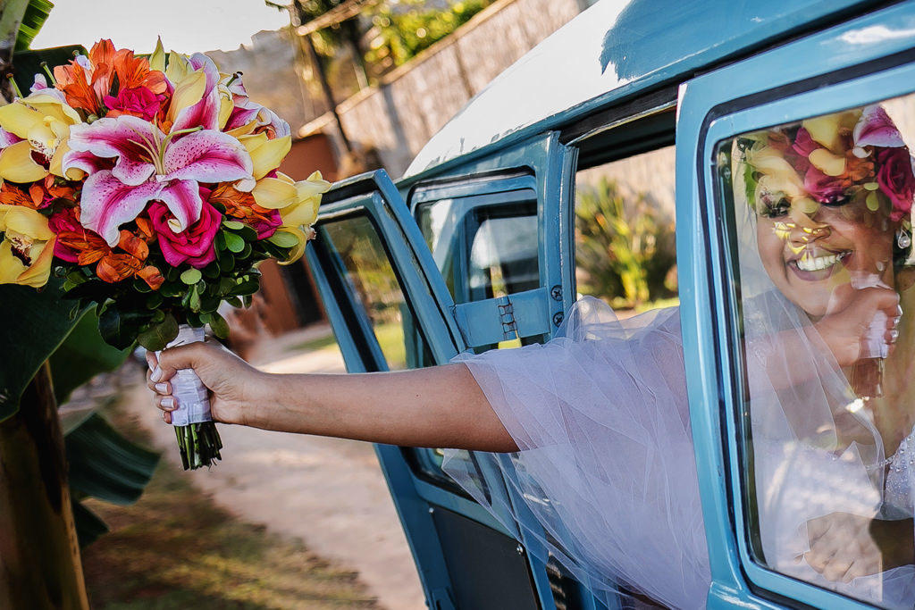 Thalita a noiva chegando ao seu casamento em uma linda kombi retro segurando o seu buque de noiva