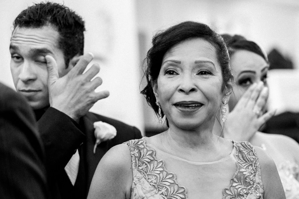 o olhar da mãe da noiva, vendo a sua filha entrando na igreja e os irmãos da noiva ao fundo enxugando as lágrimas