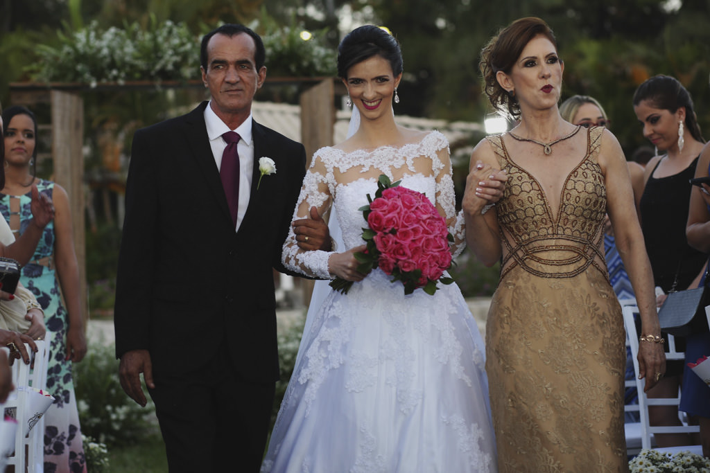 A noiva com seu lindo vestido segurando o buque entrando sorrindo com seus pais