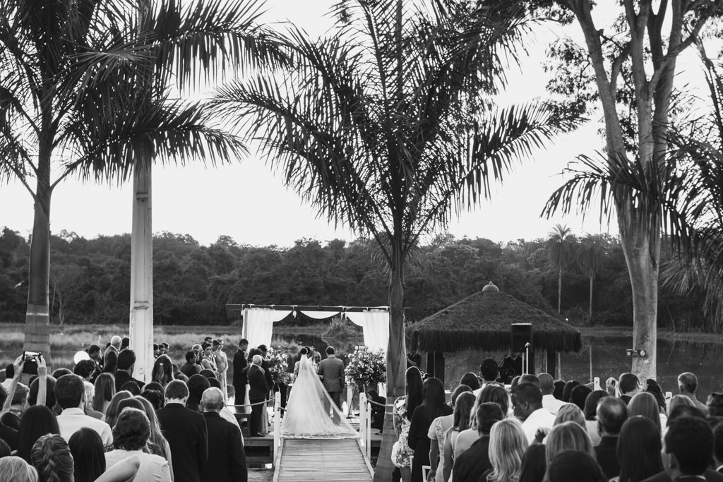 Os noivos ao fundo durante a cerimonia, mostrando todos os convidados e o altar no deck