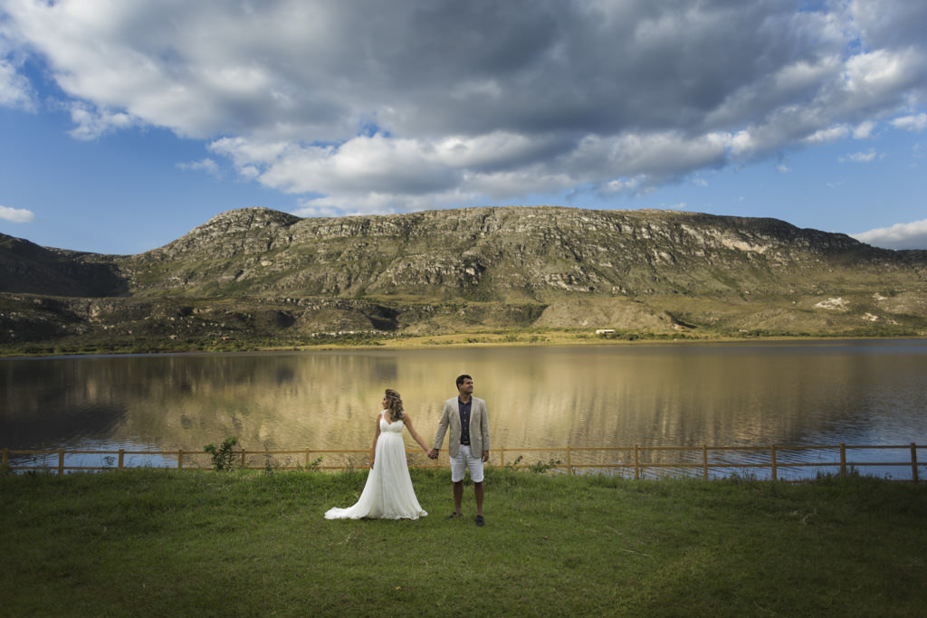 Paula com seu lindo vestido de noivo  de mãos dadas com Bruno estiloso de bermuda e terno, ao fundo a linda paisagem da Lapinha da Serra