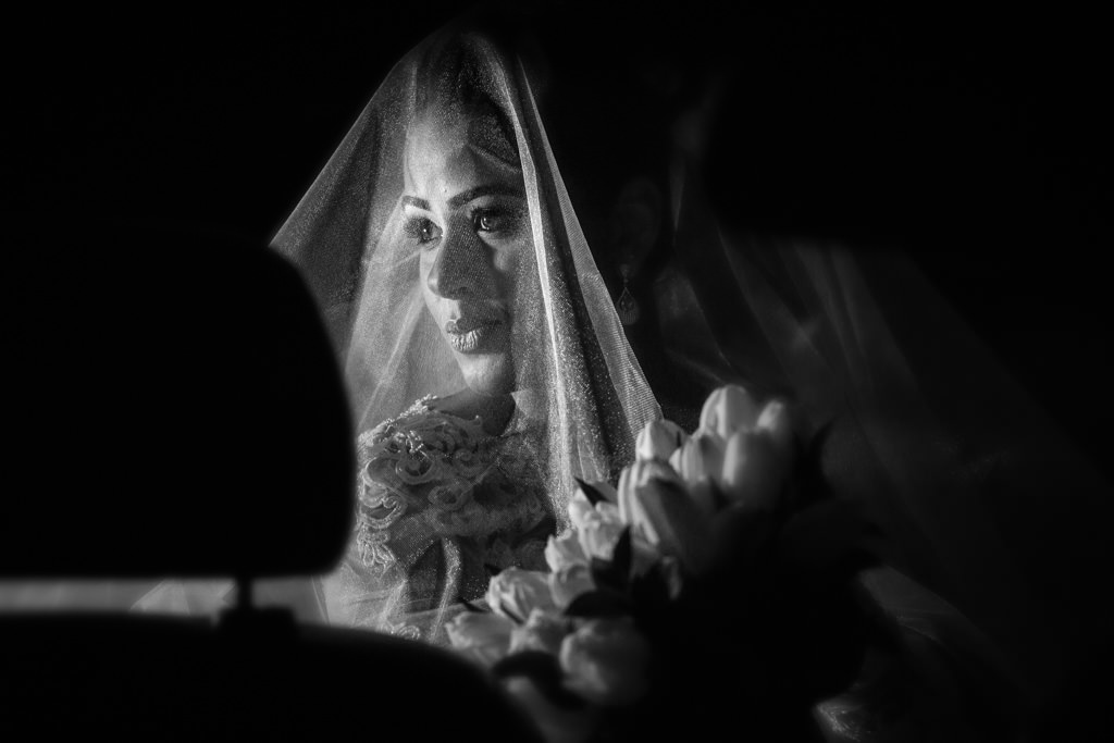 Na porta da igreja de Santana em Sete Lagoas, Nayara dentro do carro segurando seu lindo buquê  com o seu véu no rosto