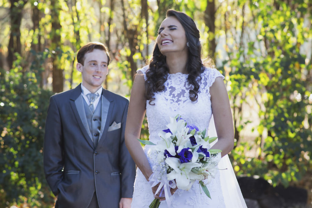 Daniela com seu lindo vestido de noiva segurando o seu buque e com um lindo sorriso sob o olhar do seu noivo Rafael