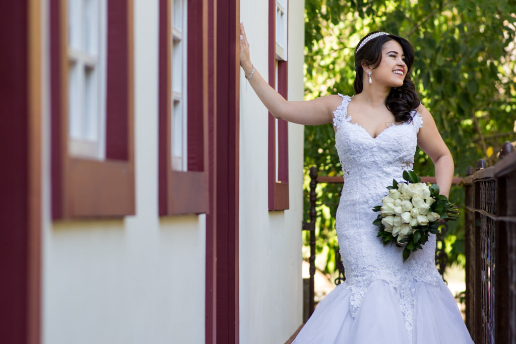 com a mão na porta marron antiga, mariana  com todo o seu charme e elegância com o seu lindo vestido de noiva segurando o seu buquê