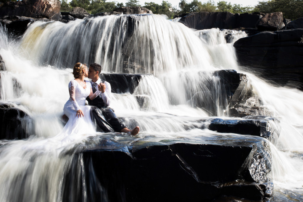 sentados nas pedra no meio da cachoeira, com a água formando um lindo véu de noiva