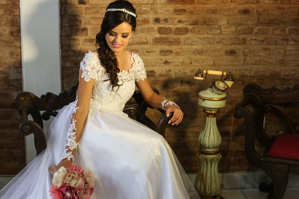 a linda noiva isabella sentada em uma cadeira estilo retrô, segurando o seu lindo buquê de noiva