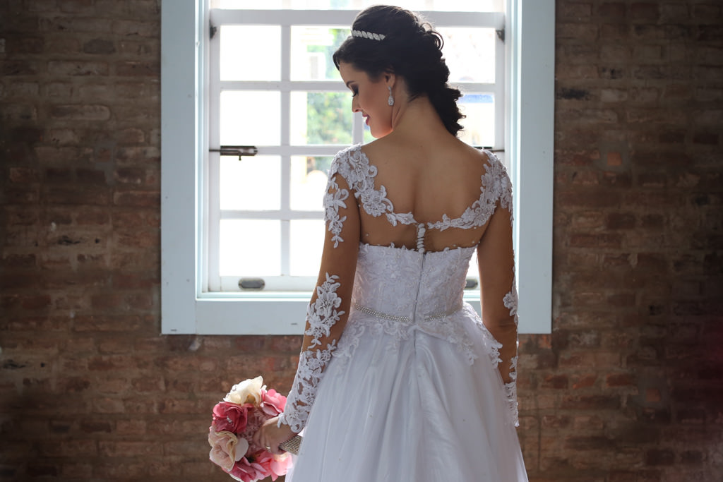com uma janela ao fundo fazendo a moldura e todos os detalhes das costas do seu lindo vestido de noiva