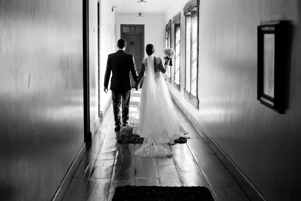 com seu lindo vestido de noiva Cassia de mãos dadas a moisés caminhado no corredor do hotel solar do engenho em sete lagoas
