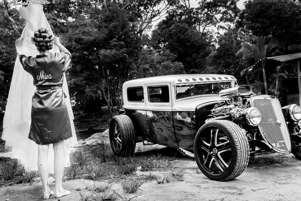 no sítio da família no Condomínio Nossa Fazenda em Belo Horizonte, a noiva Renata segurando seu vestido ao lado de um lindo hot rod