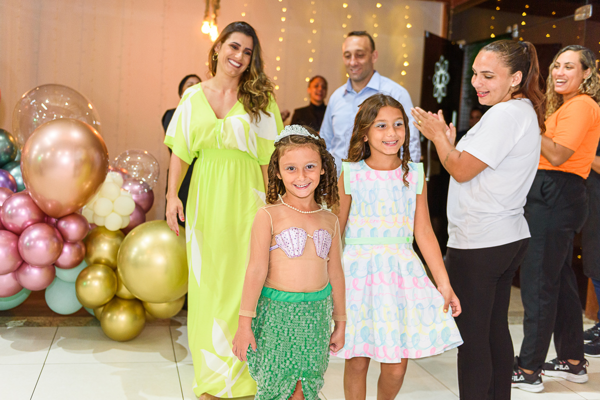 menina com roupa de sereia chega com sua irmã e seus pais