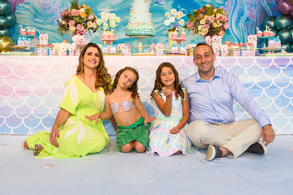 pose sentada da menina vestida de sereia com seus pais e sua irmã