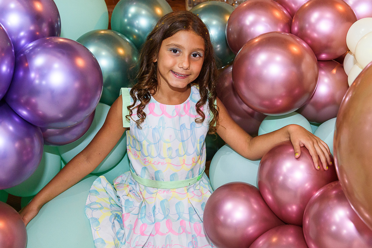 menina de vestido fazendo pose na frente de varios baloes coloridos