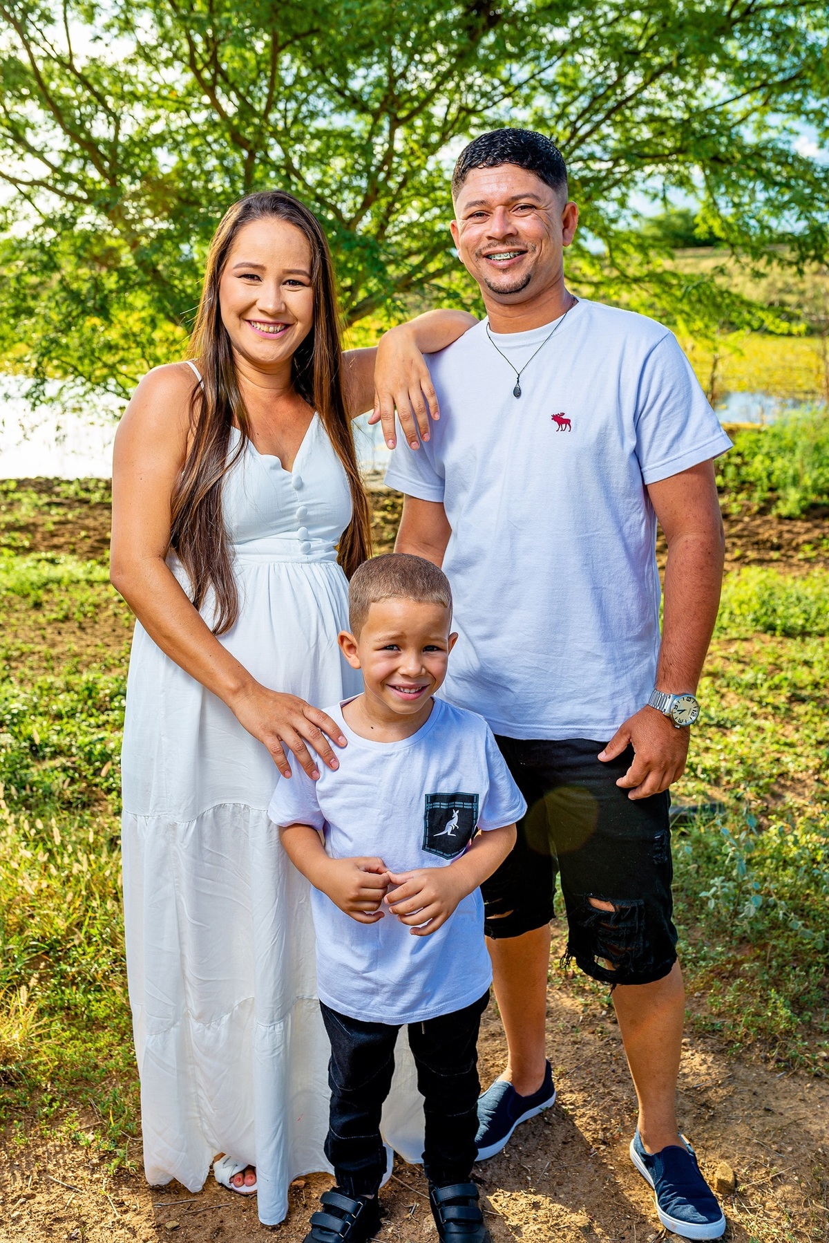 foto de uma familia em um por do sol, a mulher grávida e o filho mais velho ao centro e o marido a direita