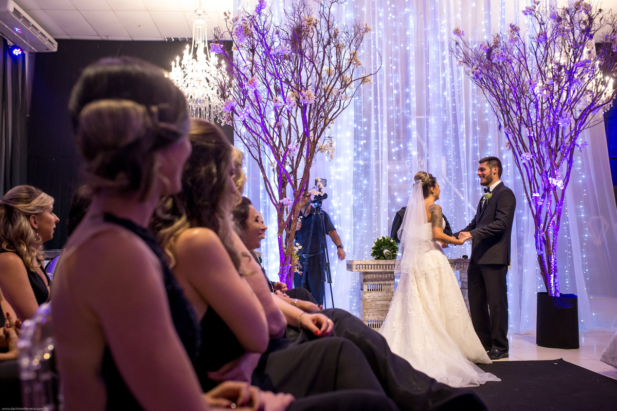 noivos no altar mãos dadas madrinhas observam