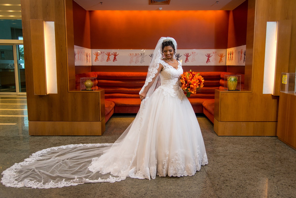 noiva negra sorri estende véu longo bordado renda buque laranja saguão hotel